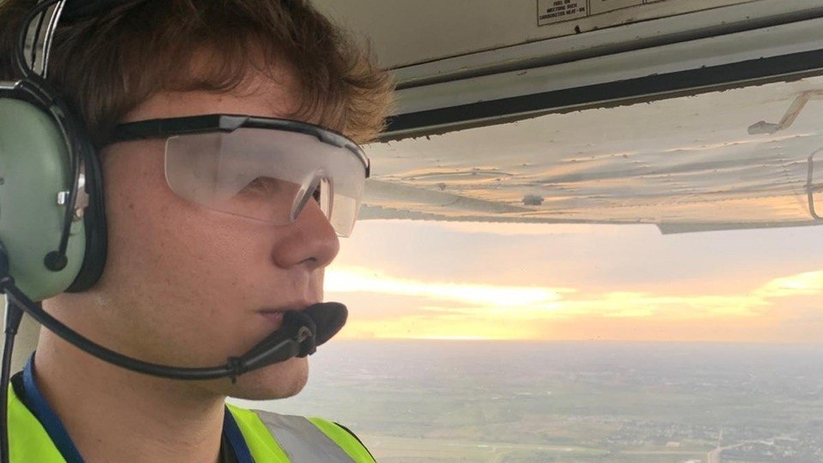 Piloto con headset en cabina durante un vuelo al atardecer, con cartillas de checklist visibles sobre la ventanilla